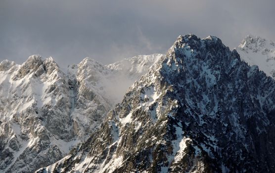 Dramatic snow-covered mountain peaks showcasing winter's icy embrace under a cloudy sky.