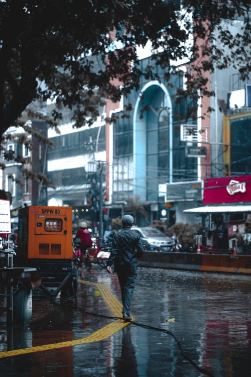 Free A person walks through a rain-soaked street in Jakarta, Indonesia, capturing urban life amidst vibrant city architecture. Stock Photo