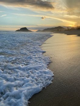 Golden sunset over a quiet beach with gentle waves and distant hills.