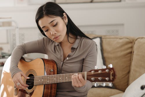 A Woman in Brown Long Sleeves Playing Acoustic Guitar