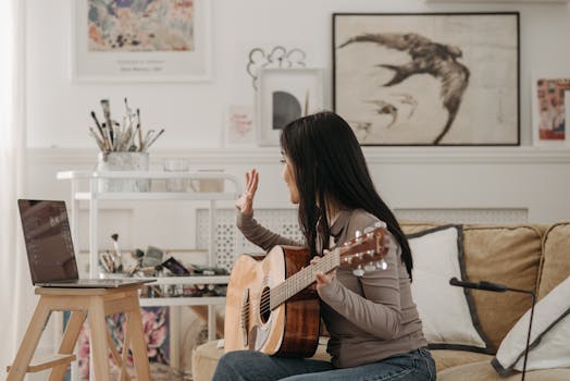 Woman playing acoustic guitar during online lesson in modern living room.