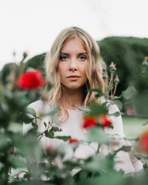 Photo of a Woman with Blond Hair Standing Near Red Flowers