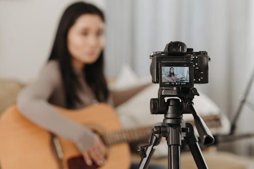 A Woman Recording with Camera while Playing the Guitar