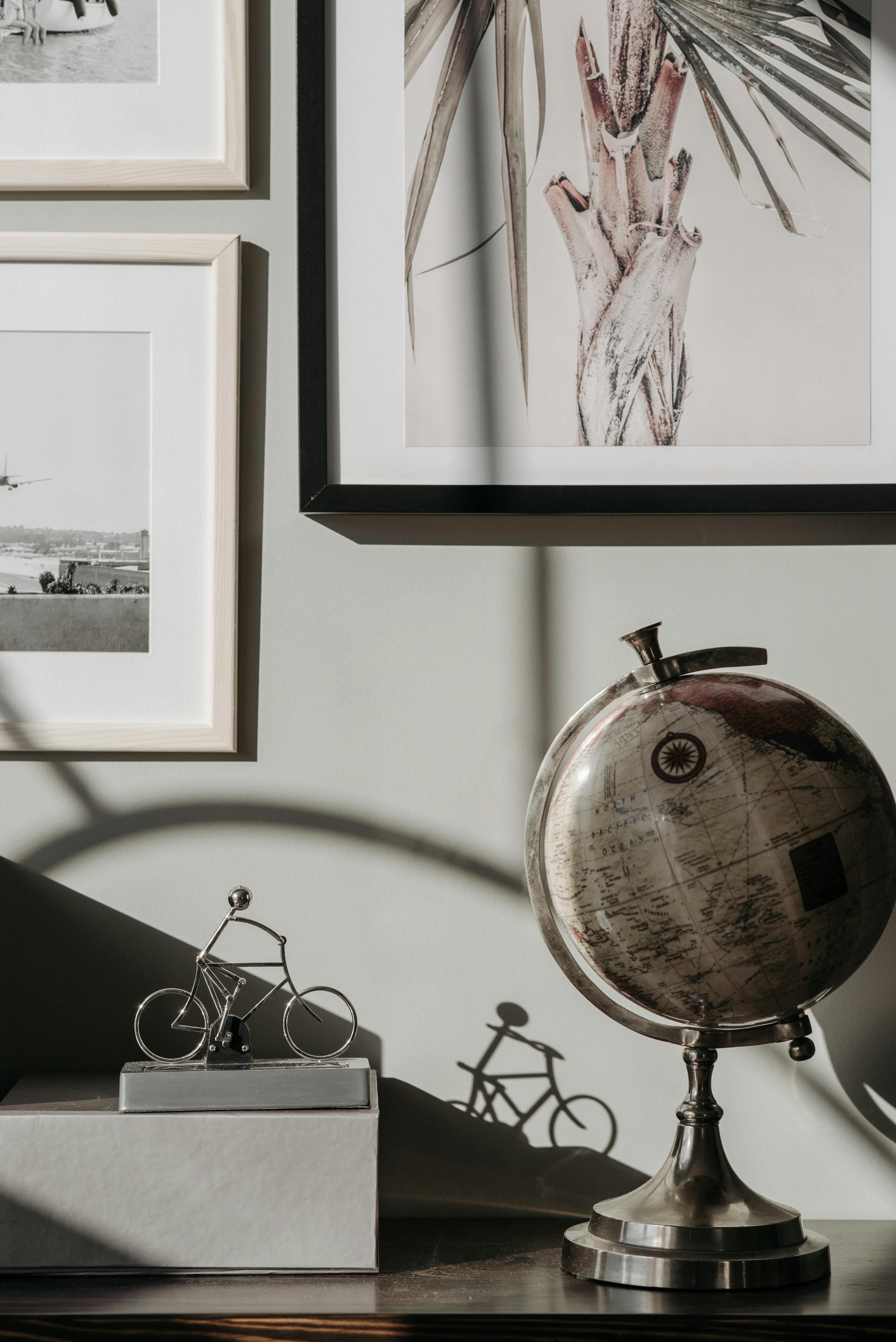 A stylish indoor scene featuring a vintage globe, framed art, and a bicycle sculpture casting a shadow.