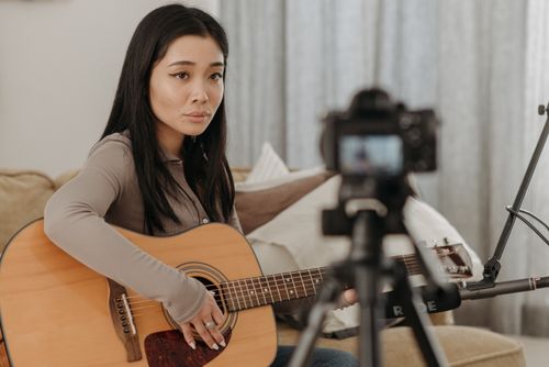 Free Asian woman playing acoustic guitar during an online music lesson at home. Stock Photo