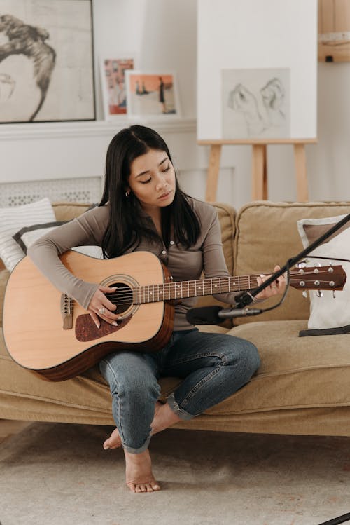 Photo of a Woman Playing an Acoustic Guitar while Sitting on a Brown Couch