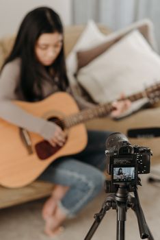 An Asian woman plays acoustic guitar while recording indoors. Perfect for music and lifestyle concepts.