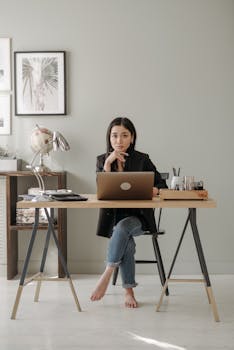 Woman working remotely at a stylish home office desk with a laptop and decor.