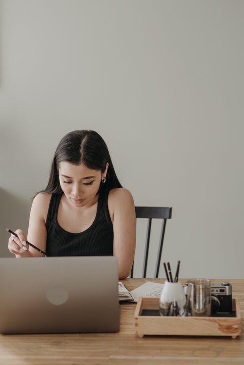 Free Asian woman at home desk engaged in online learning with laptop, notes, and pen. Stock Photo