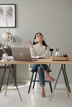 Woman sitting at a desk, wearing headphones, thinking deeply with a pencil in hand.