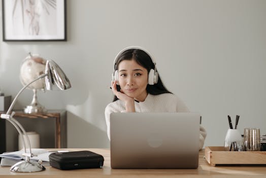 Asian woman smiling while working from home with laptop and headphones, embodying remote work lifestyle