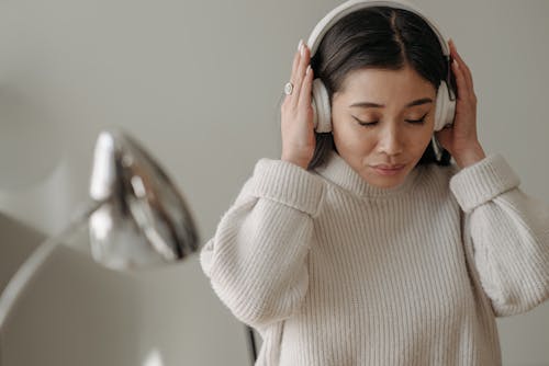 Woman in a White Knitted Sweater Wearing White Headphones