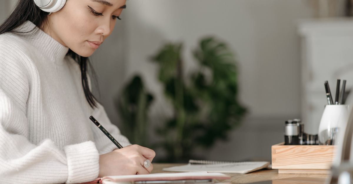 Person wearing headphones taking notes in a notebook at a desk