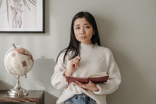 Woman in White Knit Sweater Holding Notebook and Pencil