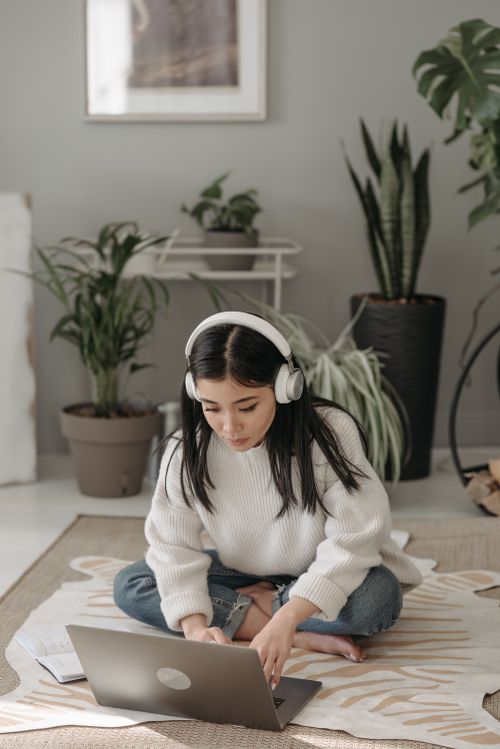 Free Focused young woman using laptop with headphones, sitting on floor, working remotely. Stock Photo