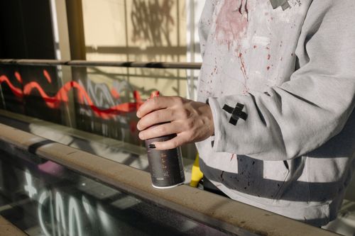 Free A street artist's hand holding a spray paint can, creating red graffiti art on a wall in an urban setting. Stock Photo