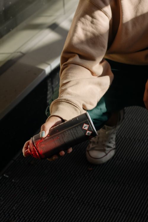 Free A person crouches indoors, holding a red spray paint can in a sunlit area. Stock Photo