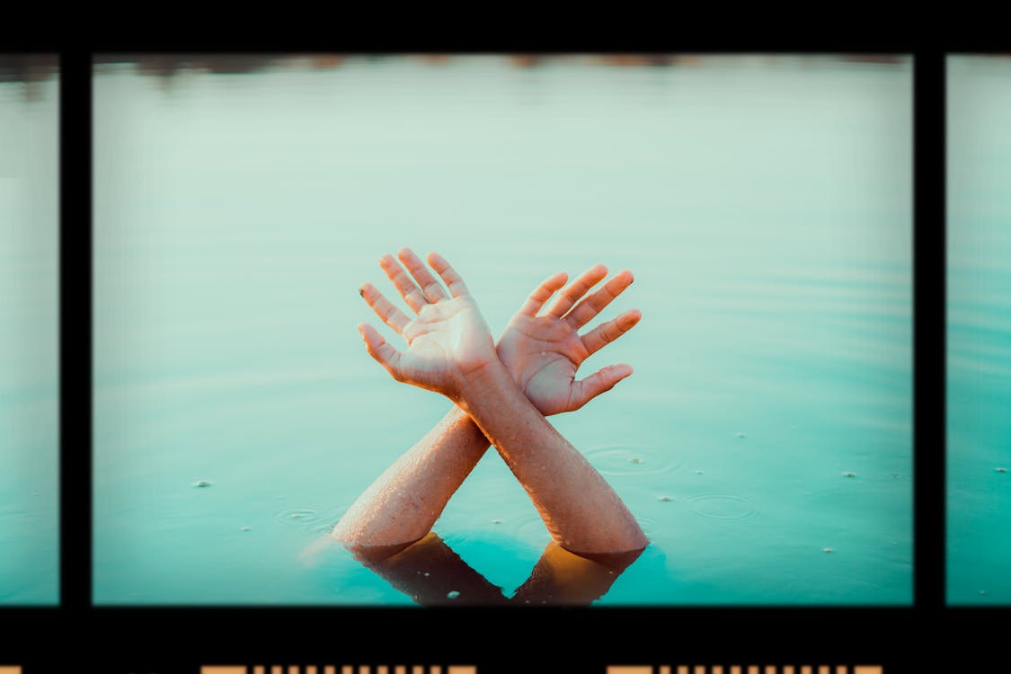 Film with photo of crop anonymous person raising hands in water in daytime