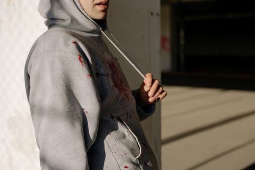 Free A close-up of a person in a gray hoodie with paint splatters in an urban setting. Stock Photo