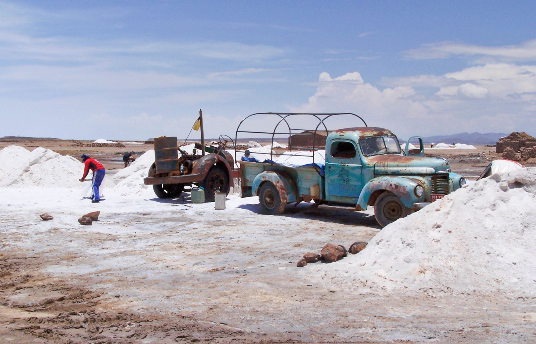 Workers extracting salt in Potosi, Bolivia, with vintage rusty truck under clear sky.
