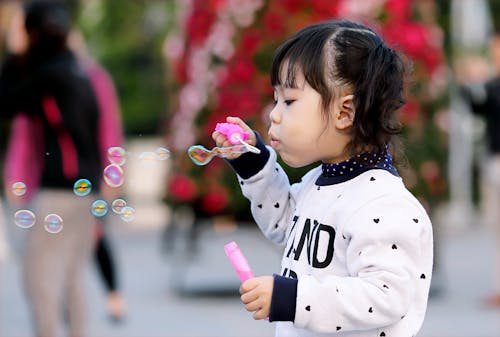 Ragazza Del Bambino Che Indossa Il Maglione Bianco E Nero Che Tiene La Bottiglia Di Plastica Delle Bolle Durante Il Giorno