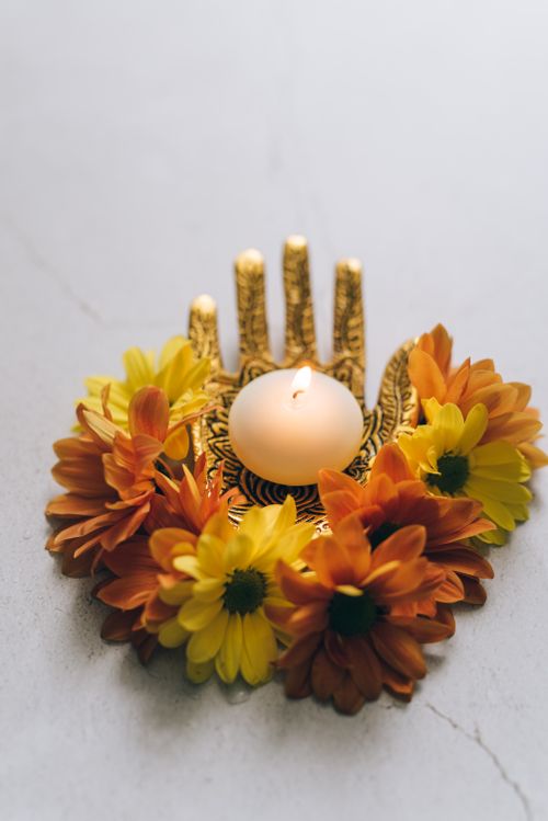 Free A lit tealight candle surrounded by colorful flowers in an ornate holder, perfect for festive decor. Stock Photo