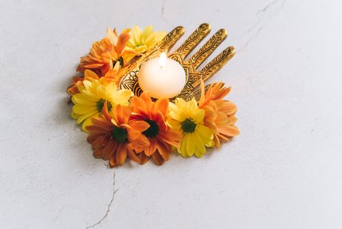 Free A lit candle surrounded by decorative yellow and orange flowers on a white surface. Stock Photo