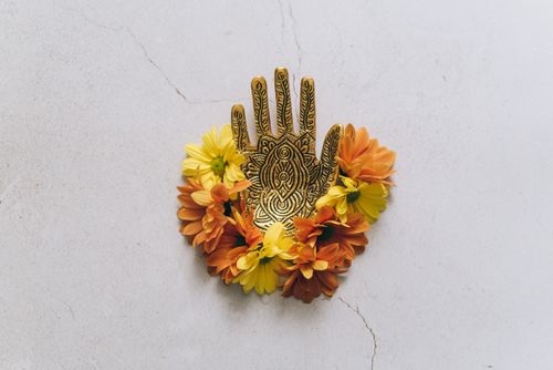 Free An intricately detailed sculpture of a hand surrounded by vibrant flowers on a textured surface. Stock Photo