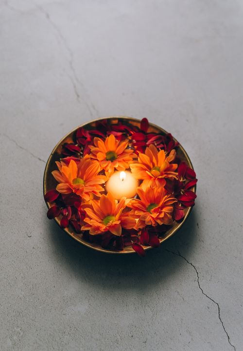 Free A glowing candle surrounded by orange and red petals in a bowl, symbolizing Diwali celebrations. Stock Photo
