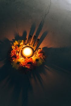 A warm Diwali decoration with a lit candle surrounded by vibrant flowers, casting shadows.