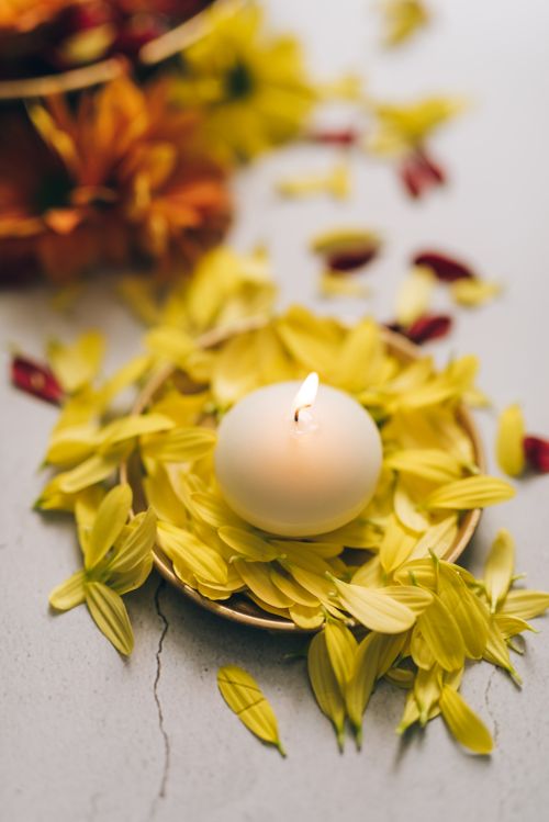 Free Lit white candle surrounded by vibrant yellow petals and flowers, ideal for Diwali decor. Stock Photo