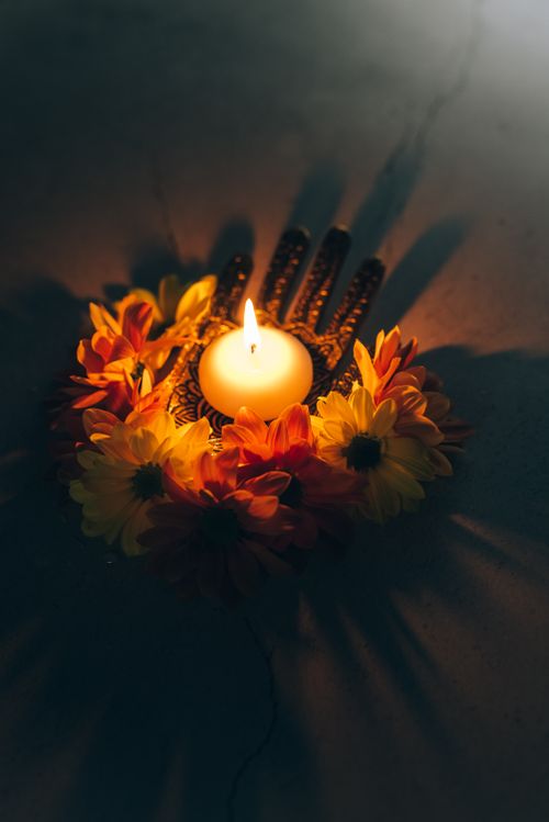 Free A glowing candle surrounded by vibrant flowers creating a serene night ambiance. Stock Photo