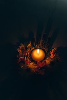 A lit candle in a decorative holder surrounded by orange and yellow flowers, symbolizing Diwali celebrations.
