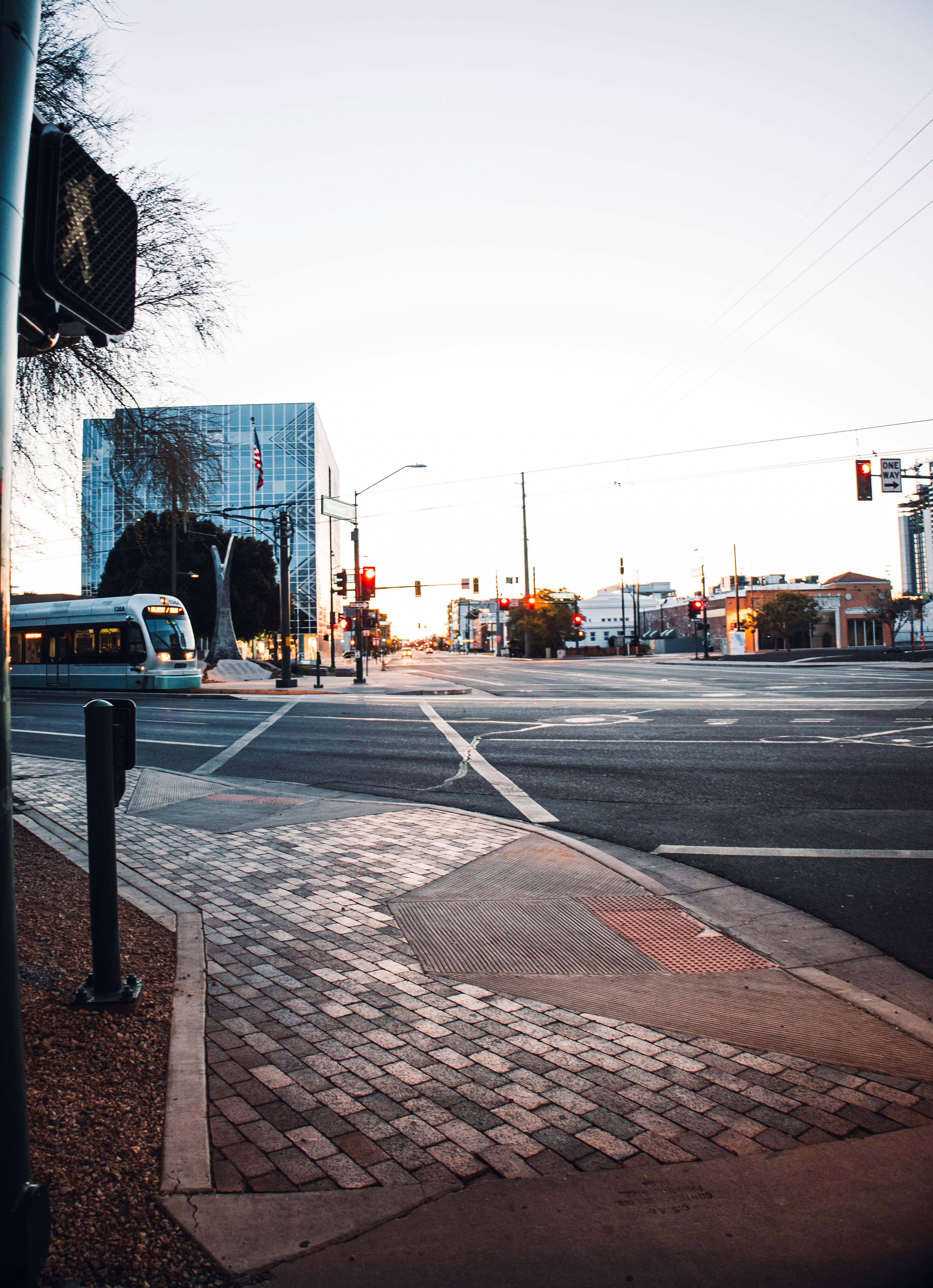A vibrant city intersection featuring modern buildings and a train, captured at dusk with striking light and shadows.