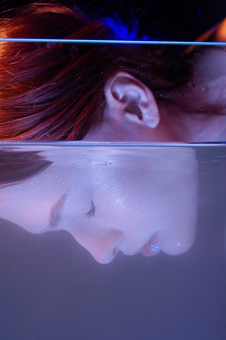 Serious Woman With Face In Glass Container With Water