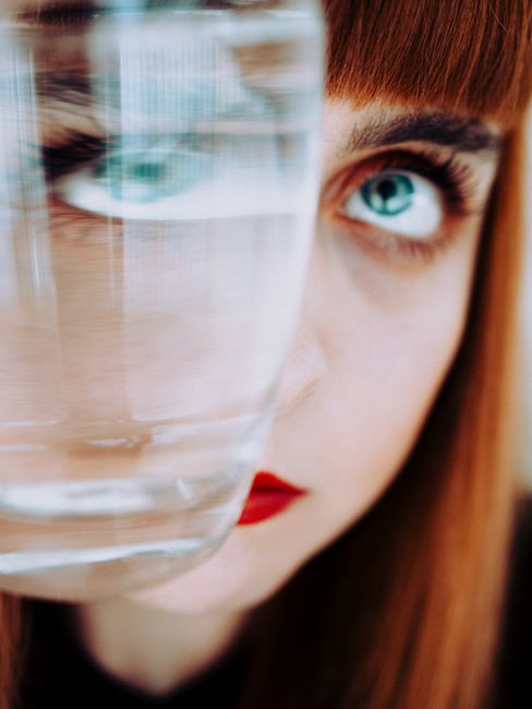 Artistic shot of a woman looking through a glass, creating a distorted perspective effect.