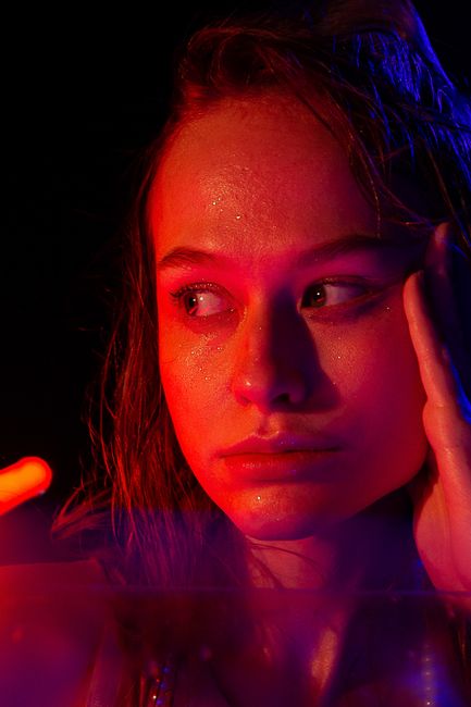 Serious young lady looking away with glowing face in dark room with orange and red neon lights