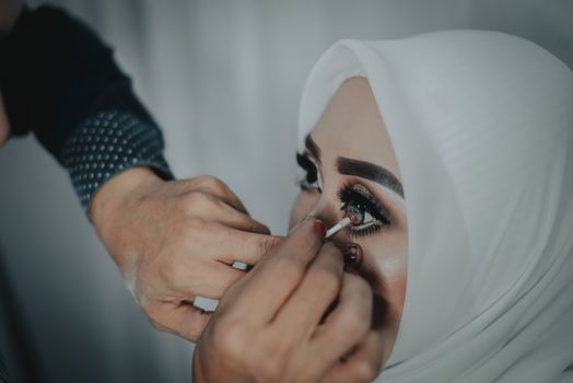 Detailed shot of eye makeup being applied to a woman wearing a hijab, showcasing cosmetic artistry.