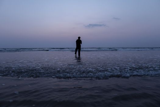 A solitary figure stands on Saligrama Beach in India as twilight paints the sky.