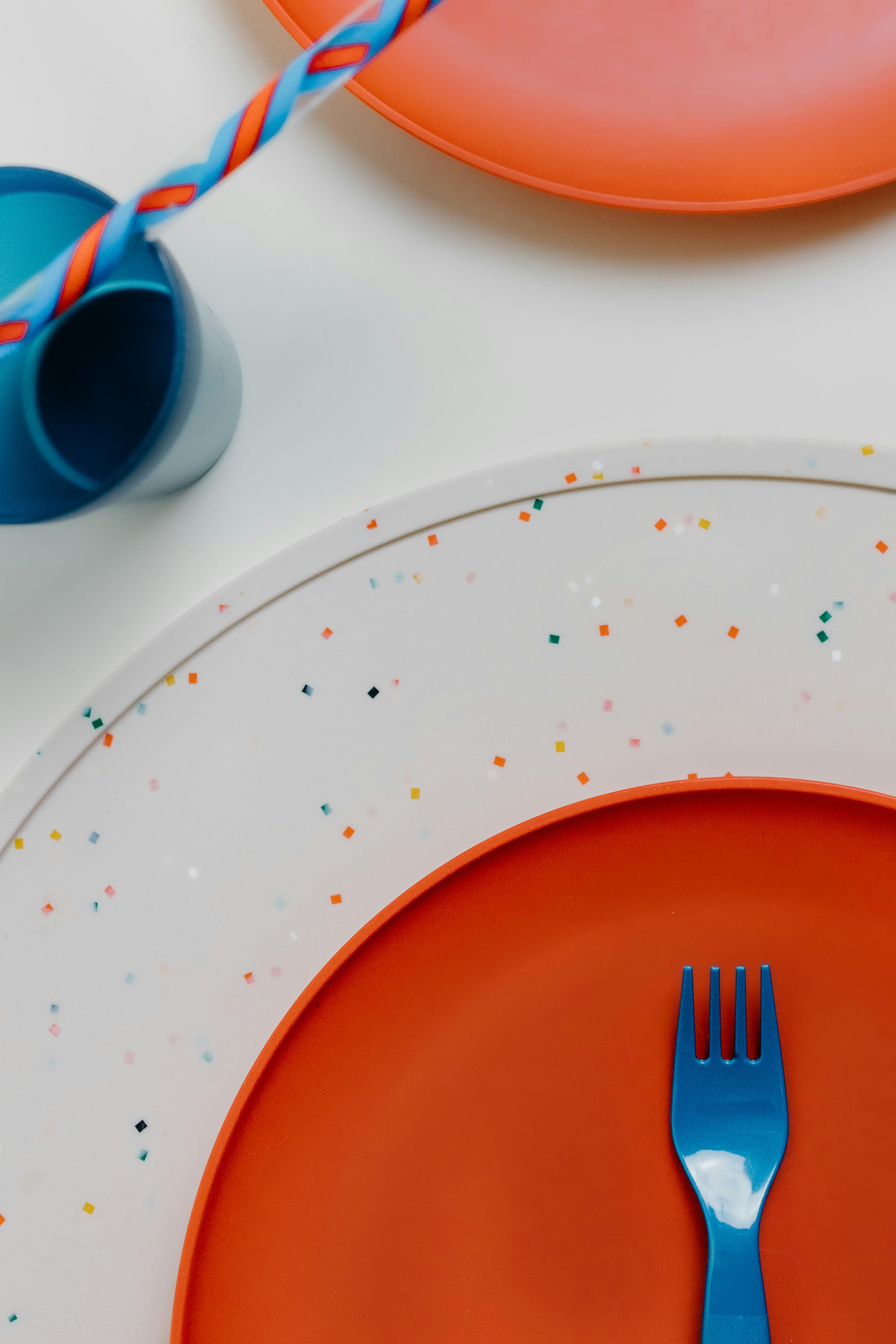 Vibrant overhead shot of colorful plates and a fork on a playful table setup.