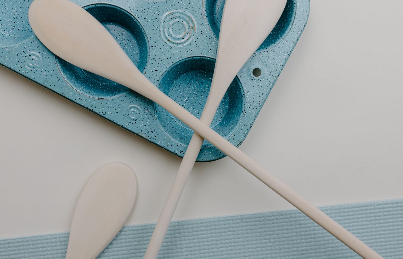 Minimalist kitchen scene with wooden spatulas and a blue baking tray on a white surface.