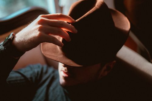 Free Elegant man with a fedora hat casts shadow over his face in a warm, artistic portrait. Stock Photo
