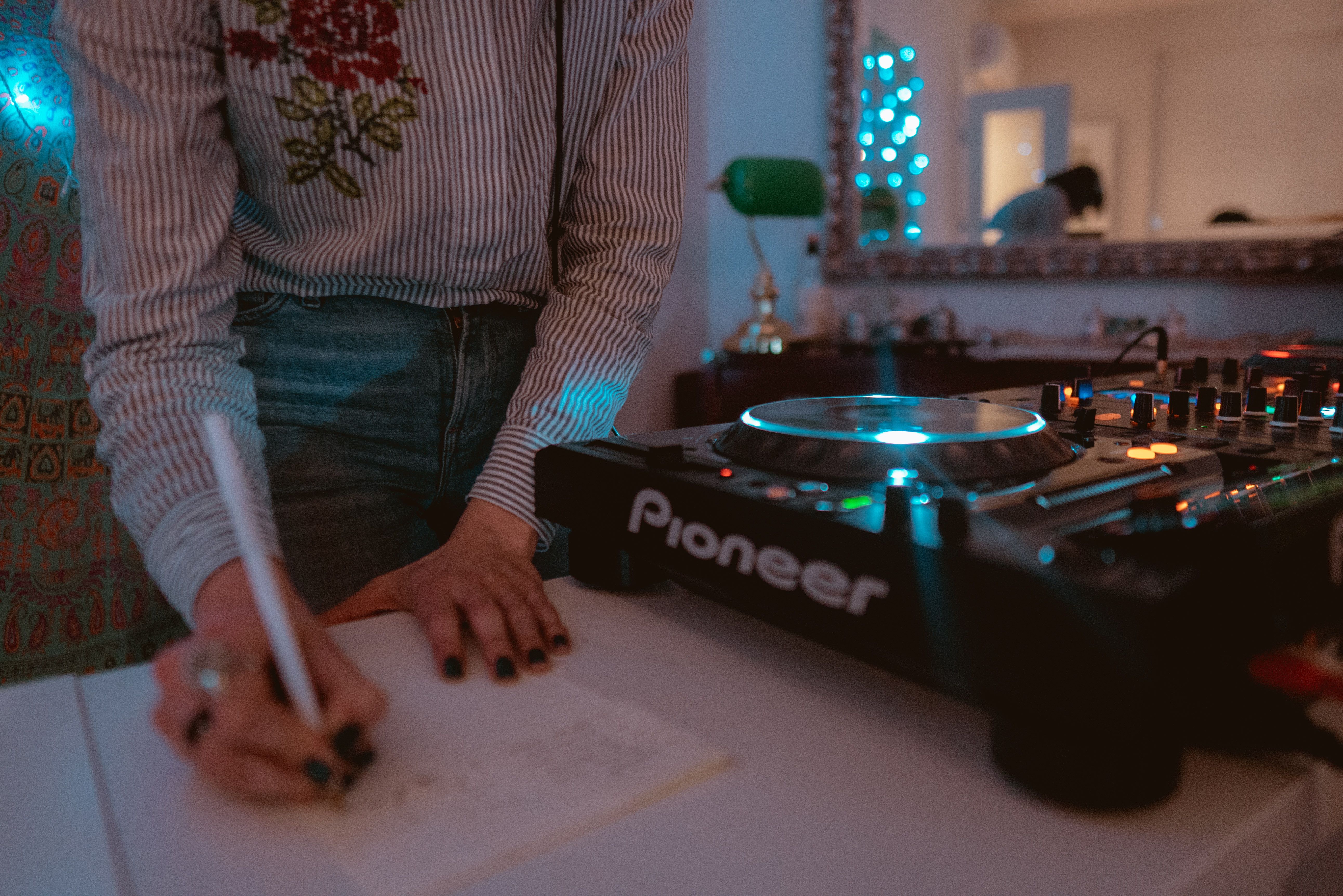 DJ writing notes beside an illuminated audio mixer