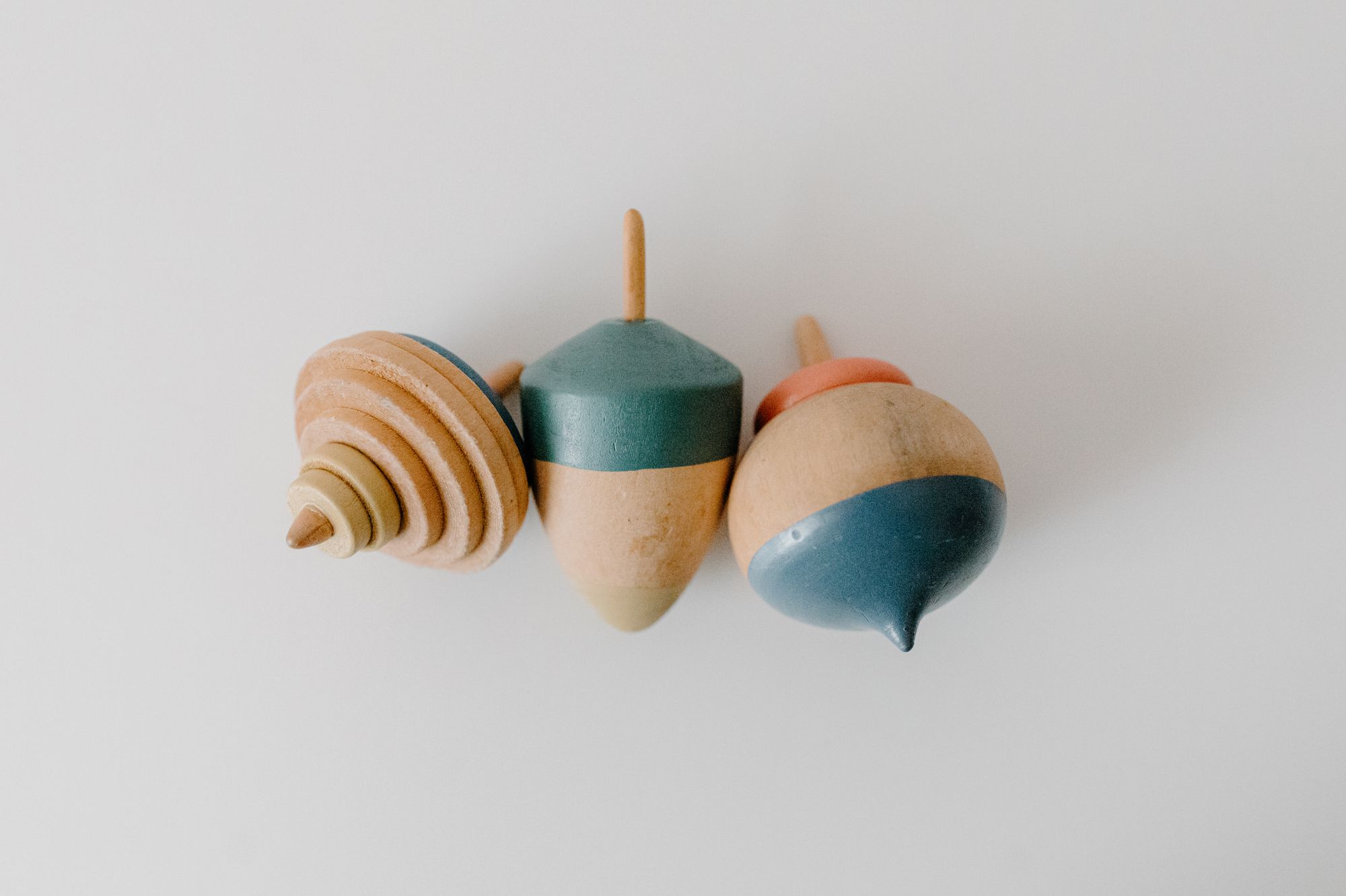 Close-up of three colorful wooden spinning tops on a white surface.