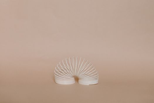 A beautifully minimalist photo featuring a white slinky set against a cream-colored background.
