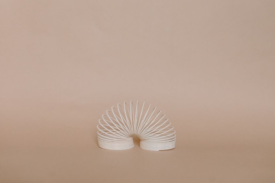 A beautifully minimalist photo featuring a white slinky set against a cream-colored background.