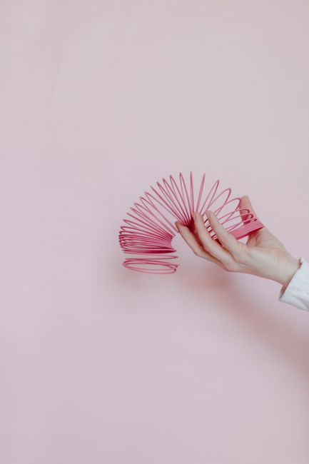A hand playing with a pink plastic slinky against a soft pastel pink background, isolated.
