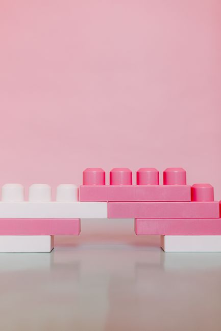 Pink and white toy building bricks stacked in a minimalist setup against a pink backdrop.
