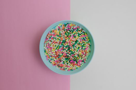 A pastel blue bowl filled with colorful sprinkles on a split pink and white background.