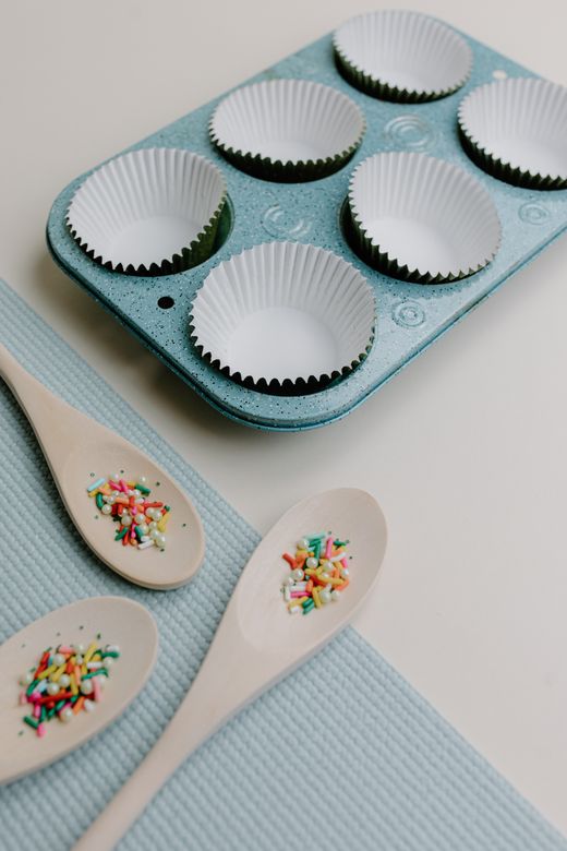 Speckled aqua muffin pan with paper liners and wooden spoons of sprinkles